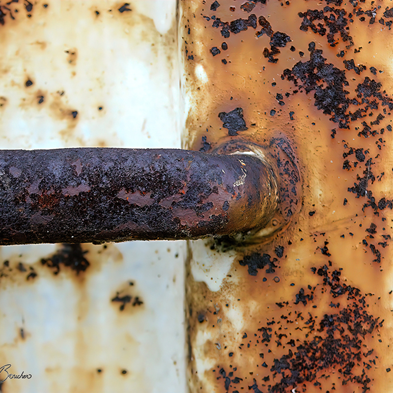 Gros plan sur une poignée métallique très oxydée fixée sur une surface orangée et crème, couverte de taches et d’écailles de corrosion, œuvre photographique de Pierre Tomy Le Boucher.