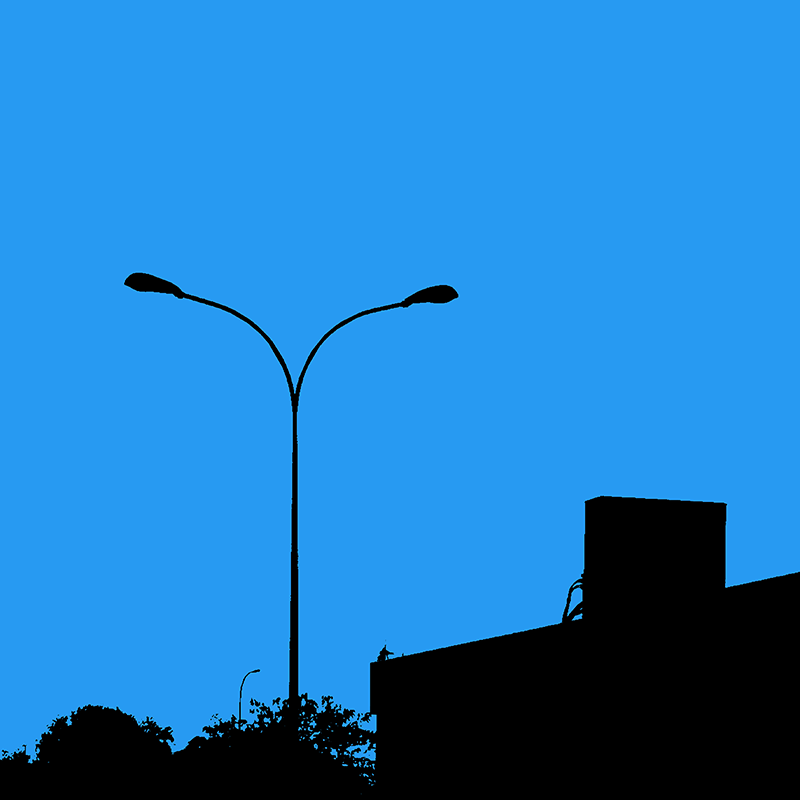 Silhouette noire d’un double lampadaire, d’une architecture et de végétation sur un ciel bleu uniforme.