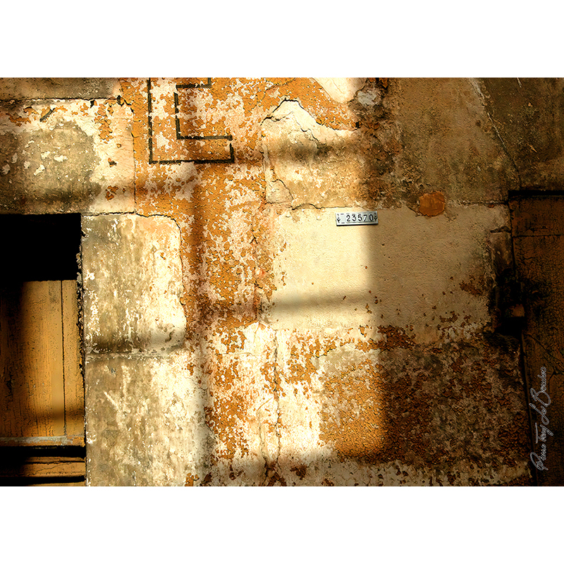Mur ancien couvert d’enduits, de peintures écaillées, de fissures et de traces ocres et grises, traversé par des zones d’ombre et de lumière, œuvre photographique de Pierre Tomy Le Boucher.
