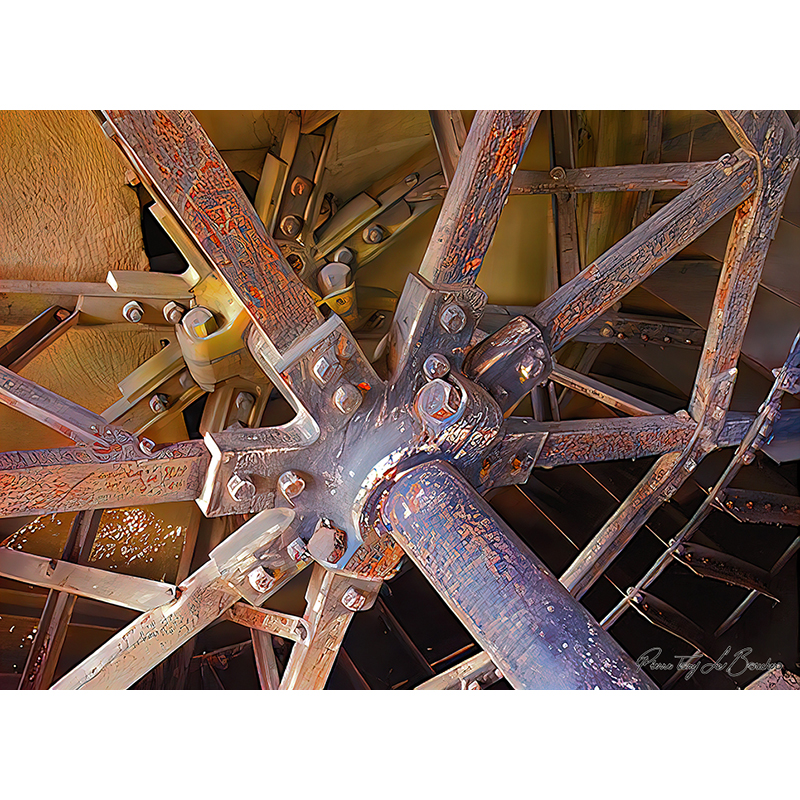 Gros plan sur une grande roue mécanique de moulin composée de bras, boulons et assemblages métalliques marqués par l’usure et l’oxydation, œuvre photographique de Pierre Tomy Le Boucher.